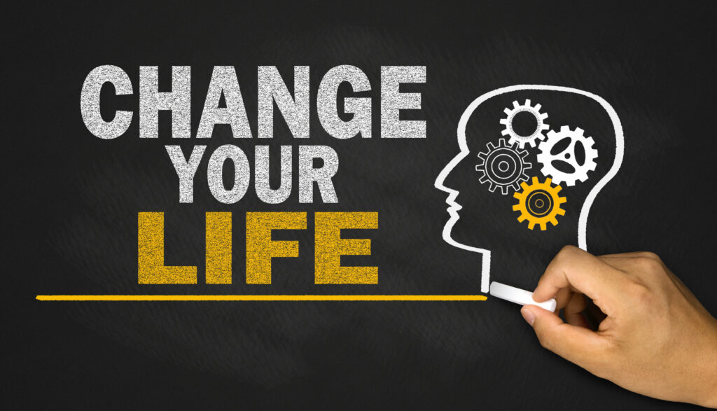 A hand completing a drawing on a chalkboard of a human head containing cog wheels looking at the legend 'change your life'.